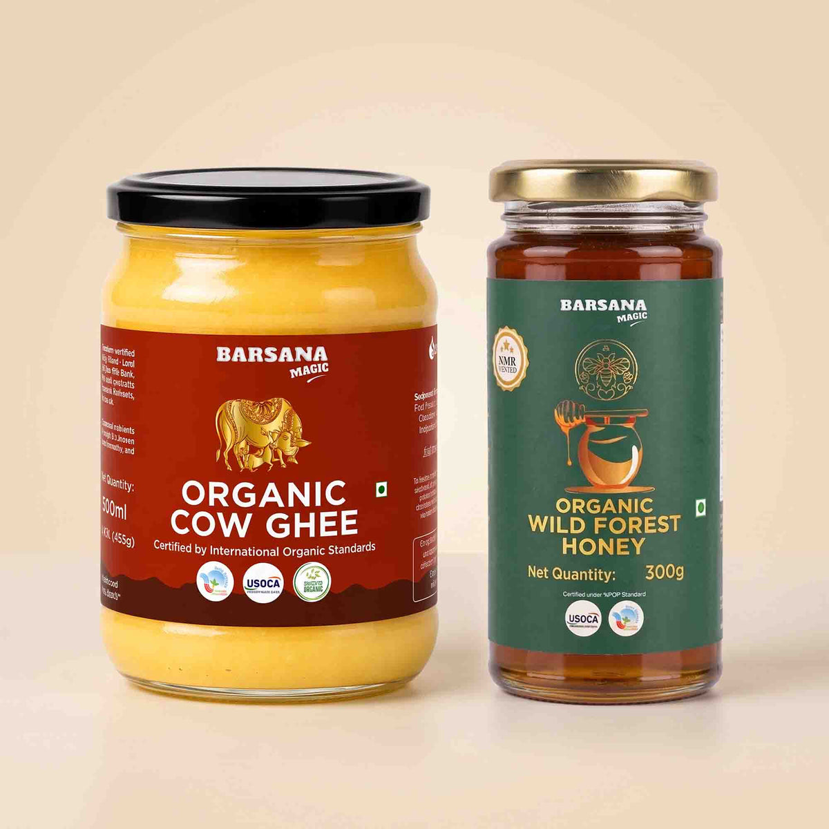 Barsana Magic and Two glass jars of organic honey and cow ghee displayed side-by-side on a light beige background. The left jar contains yellow organic cow ghee with a black lid and a dark red label.