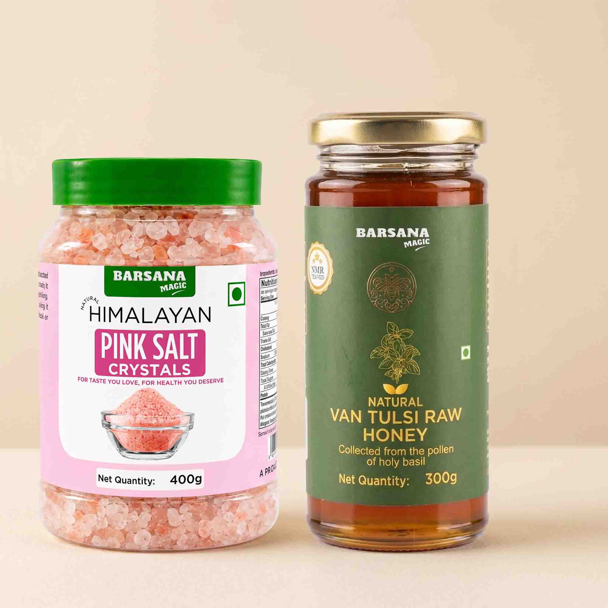 Barsana Magic and Two packaged food products on a plain beige background: a jar of Barsana Magic Himalayan Pink Salt Cystals with a green lid and pink label, and a glass jar of Barsana Magic Natural Van Tulsi Raw Honey with a gold lid and dark green label.