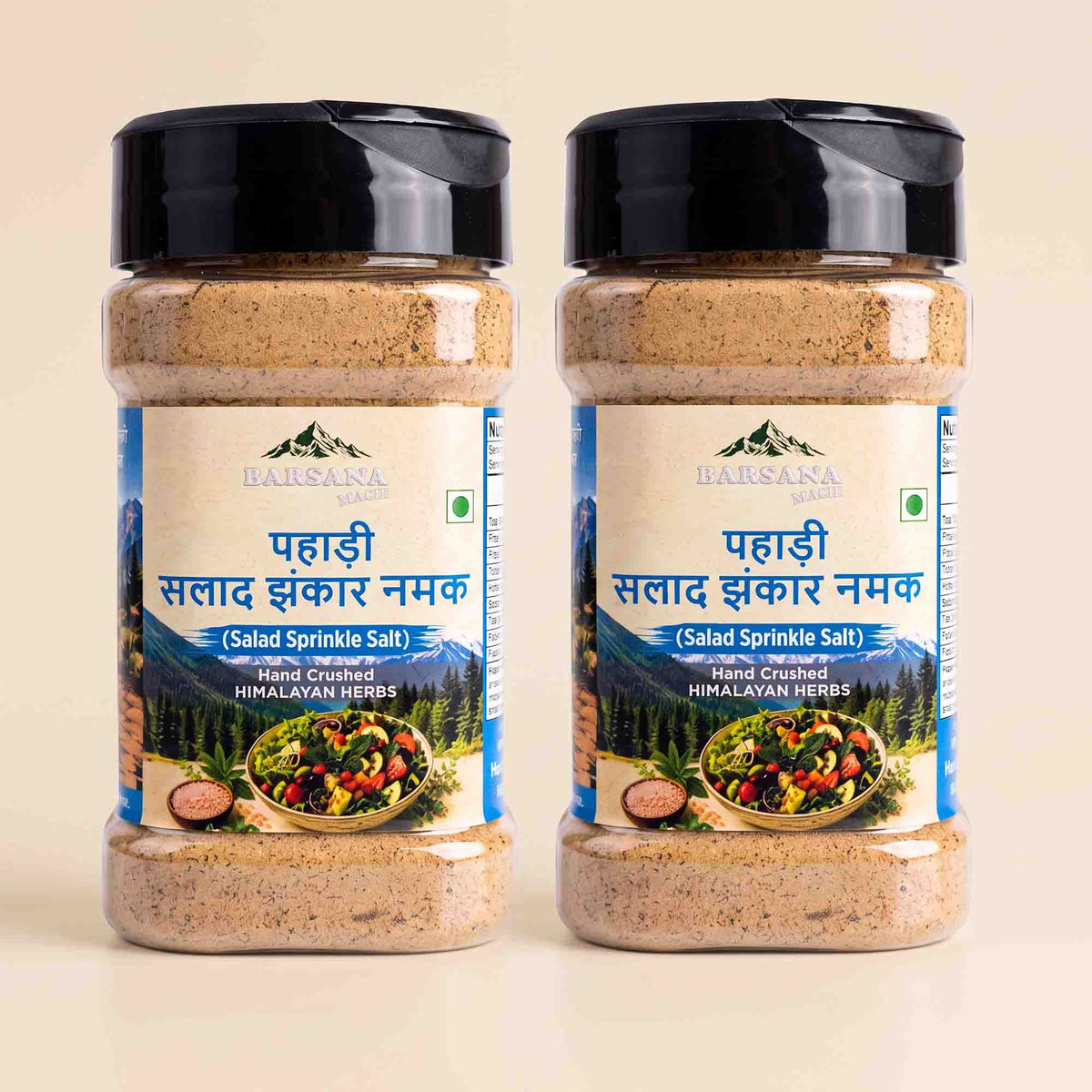 Barsana Magic and Two clear plastic jars of Barasaka Organic Hand Chopped Himalayan Herbs Salad Sprinkle Salt, filled with a beige-brown spice blend, featuring black lids and blue text on the labels, set against a light beige background.
