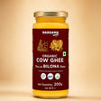 Barsana Magic andA 200g glass jar of Barsana Magic Organic Cow Ghee, made with Bilona Method, featuring a deep maroon label with gold illustrations and a gold metal lid, set against a warm beige background.
