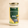 Barsana Magic and A 200g glass jar of Barsana Magic Certified Organic Buffalo Ghee, featuring a gold metal lid and a yellow and green label with a cow illustration, set against a warm beige background.