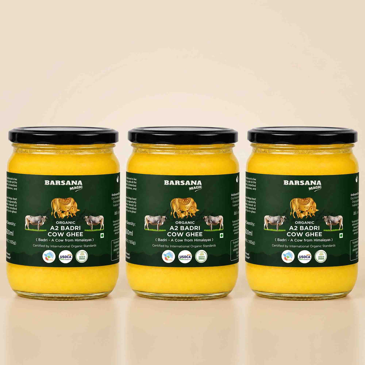 Barsana Magic and Three glass jars of Barsana Organic A2 Badri Cow Ghee arranged side by side on a light beige background. Each jar contains bright yellow ghee and has a dark green label with black lids.