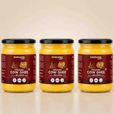 Barsana Magic and Three glass jars of Barsana Organic Cow Ghee (Rashmi and Bilona flavor) arranged side-by-side on a light beige reflective surface against a matching beige background.