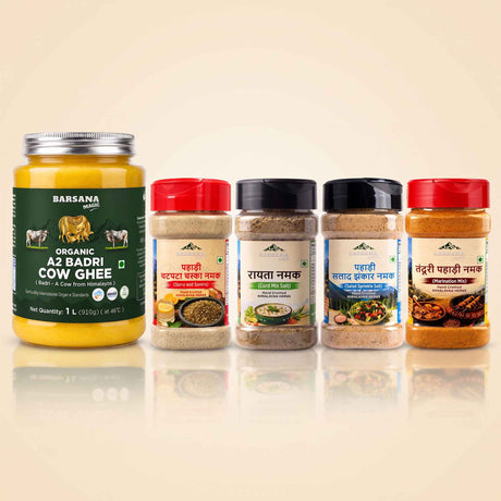 Barsana Magic and A set of BarSana brand Indian spices and ghee products displayed on a reflective beige surface against a light beige background. The set includes a large jar of BarSana Organic A2 Badri Cow Ghee on the left, and four spice jars with red, black, and white lids on the right.