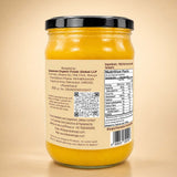 Barsana Magic and A glass jar of yellow ghee with a black lid, showing the back label with ingredients, nutrition facts, and a QR code, set against a warm beige background.