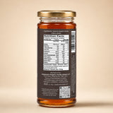 Barsana Magic and A glass jar of honey with a gold metal lid and a dark brown label showing the Nutrition Facts panel, photographed against a solid beige background.