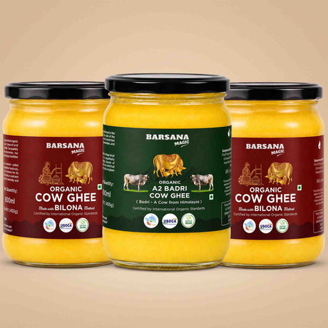 Barsana Magic and Three glass jars of Barsana Organic Cow Ghee arranged symmetrically on a warm beige background. The center jar has a dark green label, while the two side jars have dark red labels, all showing yellow ghee inside and black lids.