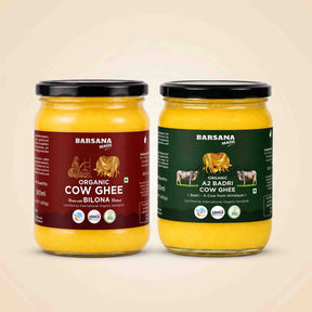 Barsana Magic and Two glass jars of Barsana Magic cow ghee on a light beige background. The left jar has a maroon label for Organic Cow Ghee and the right jar has a dark green label for Organic A2 Badri Cow Ghee, both filled with yellow ghee and topped with black lids.