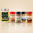 Barsana Magic and A group of Babsana brand Indian spices and ghee products arranged in a row on a reflective beige surface. The lineup includes a large jar of Certified Organic Buffalo Ghee on the left, followed by four spice jars with red, black, black, and red caps, showing various ground spices.