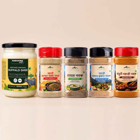Barsana Magic and Five BarSana brand spice and ghee containers arranged in a row on a light beige background. The set includes a large jar of Buffalo Ghee on the left and four spice jars with red, beige, black, and red lids on the right.