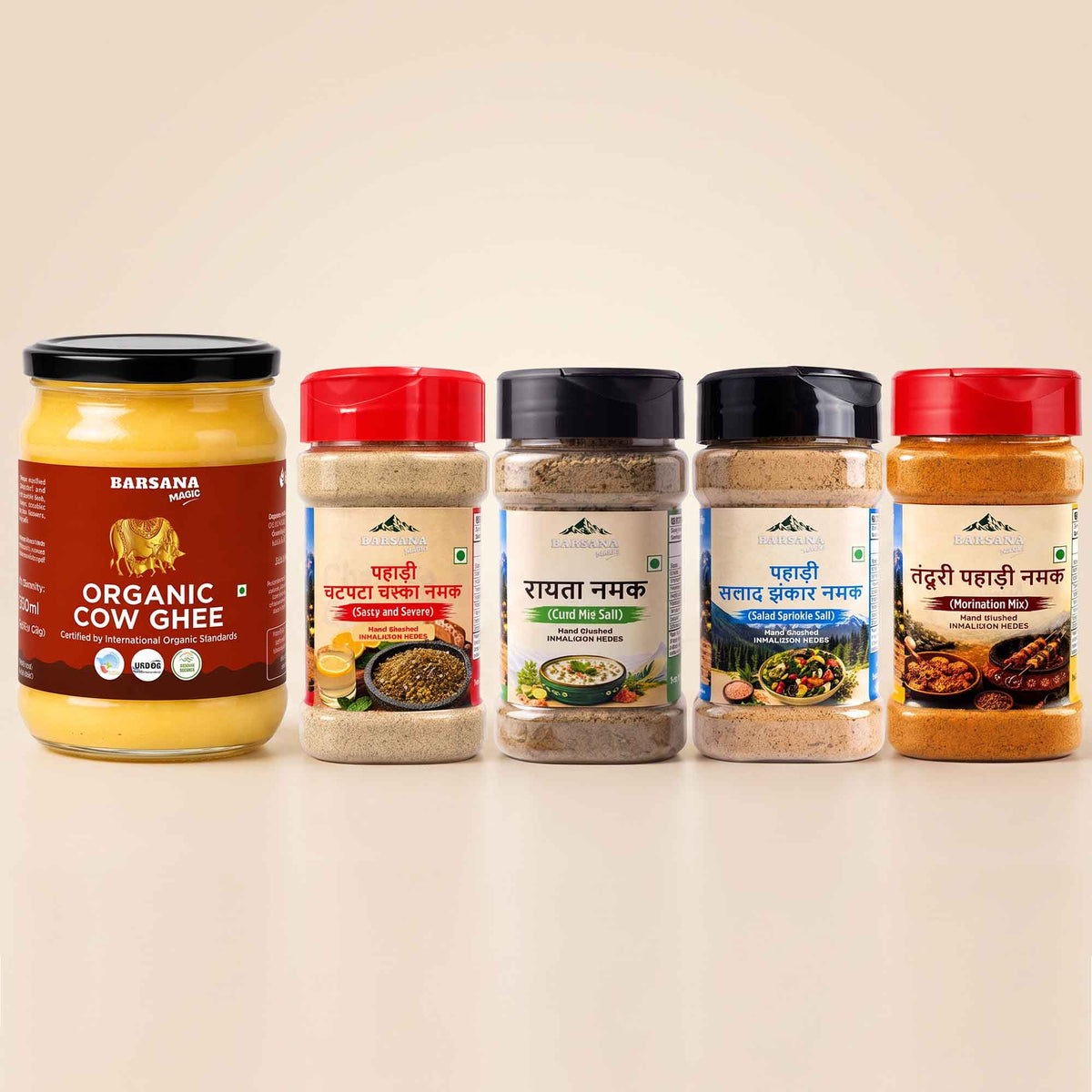 Barsana Magic and Five BARSANA brand Indian spices and ghee products arranged in a row on a light beige background. The lineup includes a large jar of Organic Cow Ghee on the left, followed by four spice jars with red, black, and dark blue lids and colorful labels.