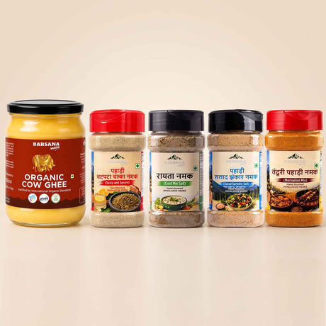 Barsana Magic and Five BARSANA brand Indian spices and ghee products arranged in a row on a light beige background. The lineup includes a large jar of Organic Cow Ghee on the left, followed by four spice jars with red, black, and dark blue lids and colorful labels.