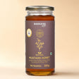 Barsana Magic and A 300g glass jar of Barsana Magic Natural Mustard Honey, featuring a dark brown label with gold lettering and illustrations, topped with a silver metal lid, set against a solid beige background.