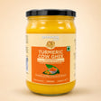 Barsana Magic and A 500ml glass jar of Barsana Turmeric Cow Ghee, showing the bright yellow ghee through the clear glass, with a cream and orange label and a black lid, set against a solid beige background.