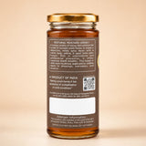 Barsana Magic and A glass jar of Natural Mustard Honey shown from the back, featuring a gold screw cap, amber-brown glass, and a detailed product label on a warm beige background.