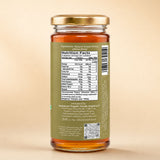 Barsana Magic and A glass jar of honey with a gold metal lid and a green label showing the nutrition facts, photographed against a solid beige background.