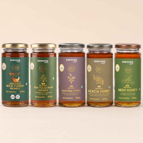 Barsana Magic and Five glass jars of brand honey arranged in a row against a light beige background. The jars contain amber-colored honey and have labels in green, purple, and brown tones with gold lettering.