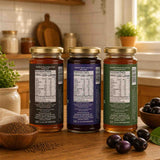 Three jars of honey with labels on a wooden table in a kitchen setting.