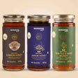 Barsana Magic and Three glass jars of Barsana Organic honey arranged side by side against a light beige background. The jars contain amber-colored honey and have distinct labels: dark brown for Awjain Honey, deep blue for Jamun Honey, and green for Van Tulsi Raw Honey.