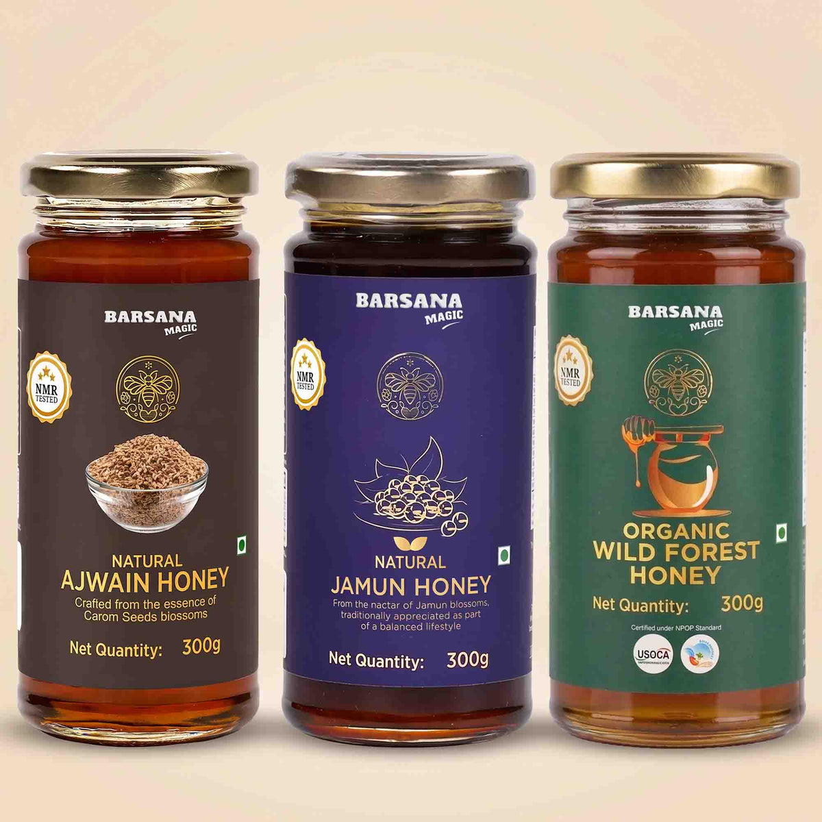 Barsana Magic and Three glass jars of Barsana Magic honey arranged side by side on a light beige background. The jars have gold lids and dark brown, deep purple, and green labels respectively, labeled Natural Ajwain Honey, Natural Jamun Honey, and Organic Wild Forest Honey.