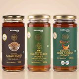 Barsana Magic and Three jars of Barsana Magic honey arranged side by side on a light beige background. The left jar is labeled Natural Ajwain Honey with a dark brown label and gold lid.