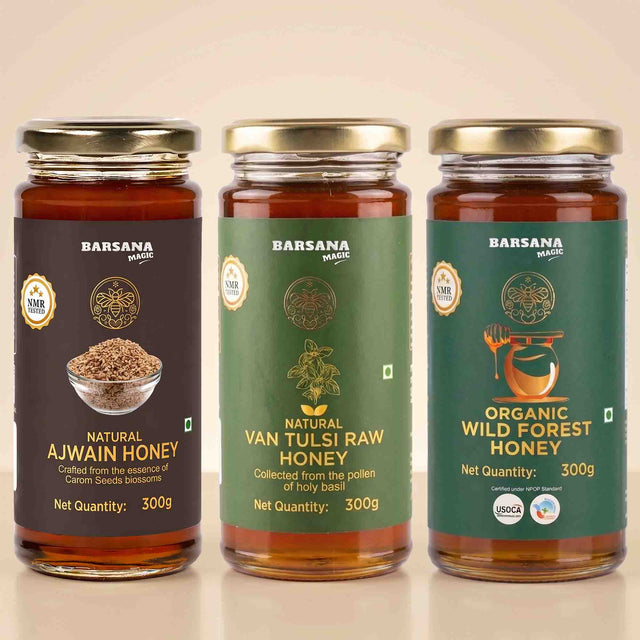 Barsana Magic and Three jars of Barsana Magic honey arranged side by side on a light beige background. The left jar is labeled Natural Ajwain Honey with a dark brown label and gold lid.