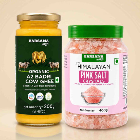 Barsana Magic and Two jars of Barsana Magic products on a light beige background: a glass jar of Organic A2 Badri Cow Ghee with a gold lid and dark green label, and a plastic jar of Himalayan Pink Salt Crystals with a green lid and pink label.
