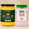Barsana Magic and Two Barsana Magic products on a beige background: a large glass jar of Organic A2 Badri Cow Ghee with a black lid and dark green label, and a plastic jar of Himalayan Pink Salt Powder with a green lid and pink label.