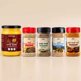 Barsana Magic and Five spice and ghee jars arranged in a row on a light beige background. The leftmost jar is a large glass jar of Barsana Organic Cow Ghee with a yellow contents and dark red label.