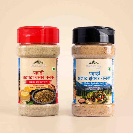Barsana Magic and Two jars of Himalayan Herb ground spices on a light beige background. The left jar has a red lid and is labeled 'Pahadi Chappata Masala Namak' (Spicy and Savory), and the right jar has a black lid and is labeled 'Pahadi Salad Zikkar Namak' (Salad Sprinkle Salt).