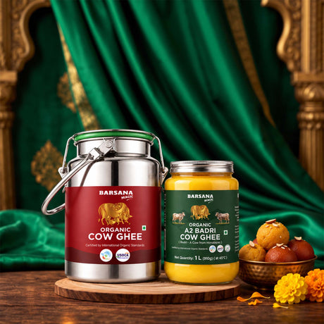 Barsana Magic and Two Barsana brand containers of Organic Cow Ghee are displayed on a wooden stand. The larger stainless steel container on the left has a red label and a green lid, while the smaller glass jar on the right has a dark green label and shows yellow ghee inside.