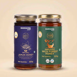 Barsana Magic and Two glass jars of Barsana Magic honey on a warm beige background. The left jar is labeled 'Natural Jamun Honey' with a dark blue label, and the right jar is labeled 'Organic Wild Forest Honey' with a green label.