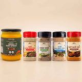 Barsana Magic and Five packaged food products arranged on a light beige background: a large jar of Barsana Masala Dairy Spread on the left, and four spice or seasoning jars with red, black, and dark lids on the right. The products are shown cleanly with no people or real environment.
