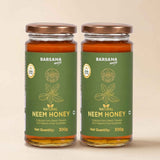 Barsana Magic and Two glass jars of Barsana Magic Natural Neem Honey with green labels and copper-colored lids, set against a solid beige background.