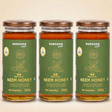 Barsana Magic and Three glass jars of Barsana Natural Neem Honey arranged side by side on a light beige background. Each jar has a dark green label with gold text and illustrations, topped with a metallic bronze lid.