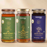 Barsana Magic and Three glass jars of Barsana Magic honey arranged side by side on a beige background. The jars are labeled Natural Neem Honey, Natural Van Tulsi Raw Honey, and Natural Jamun Honey, with green, gold, and blue labels respectively.