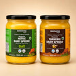 Barsana Magic and Two 500 ml glass jars of Barsana Magic dairy spreads on a beige background. The left jar contains Organic Nettle Dairy Spread with a green label, and the right jar contains Organic Turmeric Dairy Spread with a brown label.