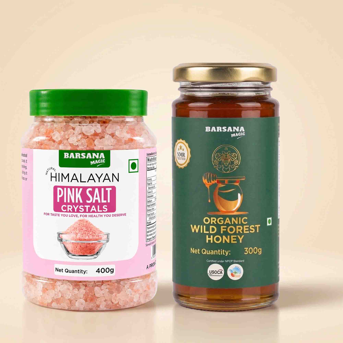 Barsana Magic and Two BarSana Magic products on a beige background: a 400g jar of Himalayan Pink Salt Cystals with a green lid and pink label, and a 300g glass jar of Organic Wild Forest Honey with a gold lid and dark green label.