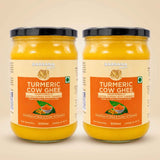 Barsana Magic and Two 500ml glass jars of Barsana Organic Turmeric Cow Ghee side by side on a light beige background. The jars contain a bright yellow-orange ghee and are fitted with black lids, featuring cream and orange labels with product details.