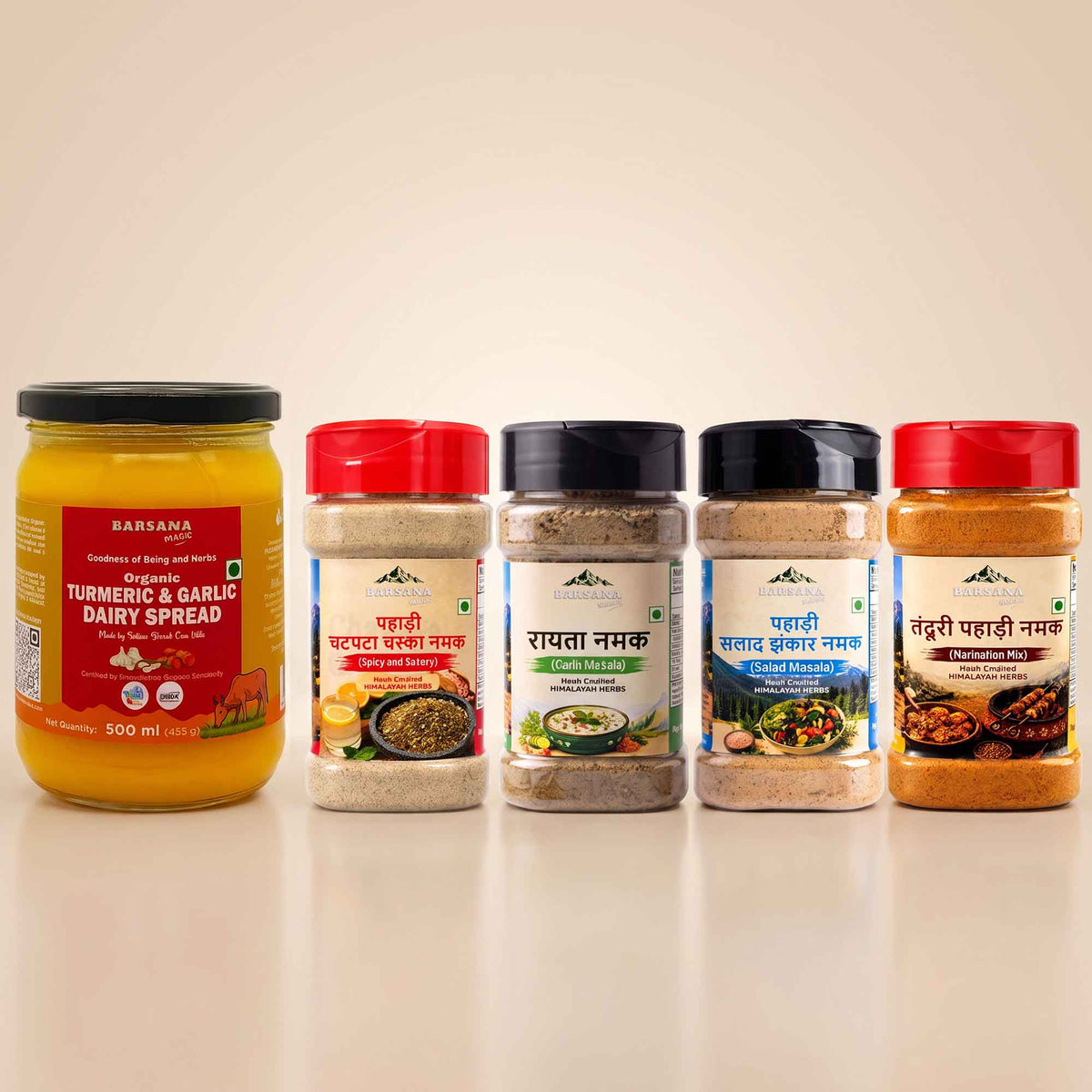 Barsana Magic and Five packaged food products arranged on a light beige studio background: a large jar of Baranka Turmeric & Garlic Dairy Spread on the left, and four spice or seasoning containers with red, black, and white lids in the center and right. No people, animals, or real environment are present, so this is Product/Packaging.