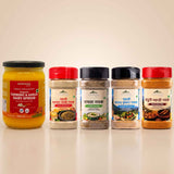 Barsana Magic and Five packaged food products arranged on a light beige studio background: a large jar of Baranka Turmeric & Garlic Dairy Spread on the left, and four spice or seasoning containers with red, black, and white lids in the center and right. No people, animals, or real environment are present, so this is Product/Packaging.
