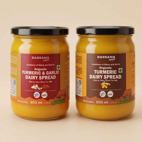 Barsana Magic and Two jars of Barsana Organic Turmeric & Garlic Dairy Spread on a warm beige background. The jars are filled with a thick yellow-orange spread and feature brown and red labels with black lids.
