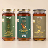 Barsana Magic and Three glass jars of Barsana brand honey arranged side by side on a light beige background. The left jar is labeled Natural Van Tulsi Raw Honey with a green label and gold lid.