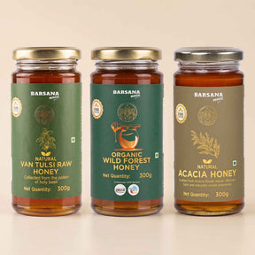 Barsana Magic and Three glass jars of Barsana brand honey arranged side by side on a light beige background. The left jar is labeled Natural Van Tulsi Raw Honey with a green label and gold lid.