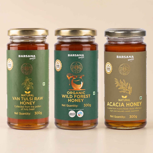 Barsana Magic and Three glass jars of Barsana brand honey arranged side by side on a light beige background. The left jar is labeled Natural Van Tulsi Raw Honey with a green label and gold lid.