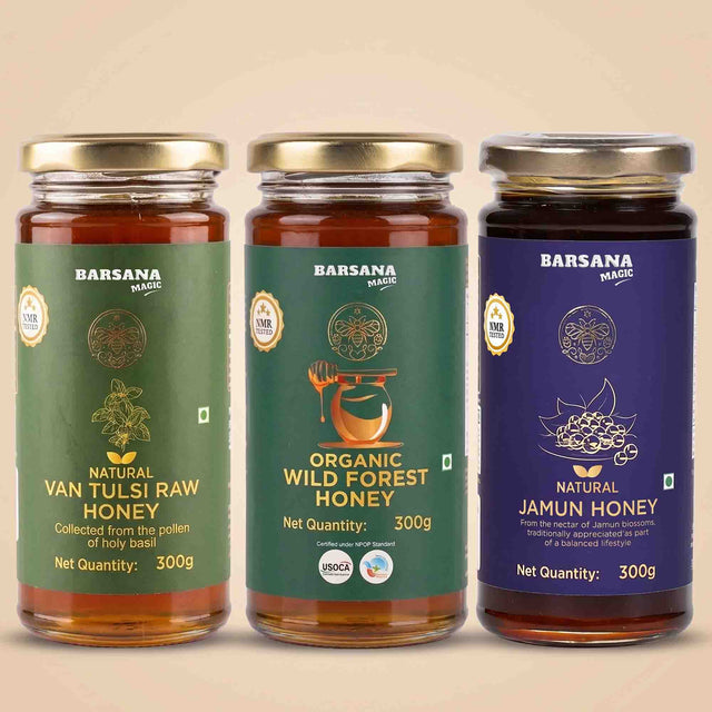 Barsana Magic and Three glass jars of Barsana Magic honey products lined up against a solid beige background. The jars contain amber-colored honey and are fitted with gold lids.