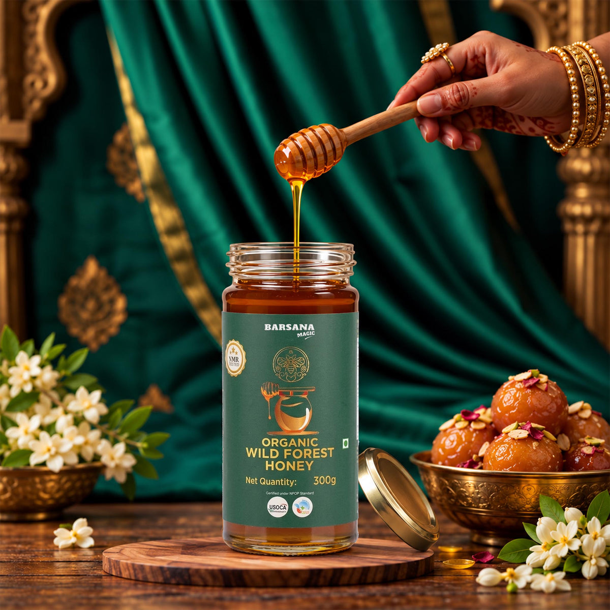 Barsana Magic and A jar of Barsana Organic Wild Forest Honey is shown on a wooden surface with honey dripping from a wooden dipper into the jar. A hand with henna is visible holding the dipper.