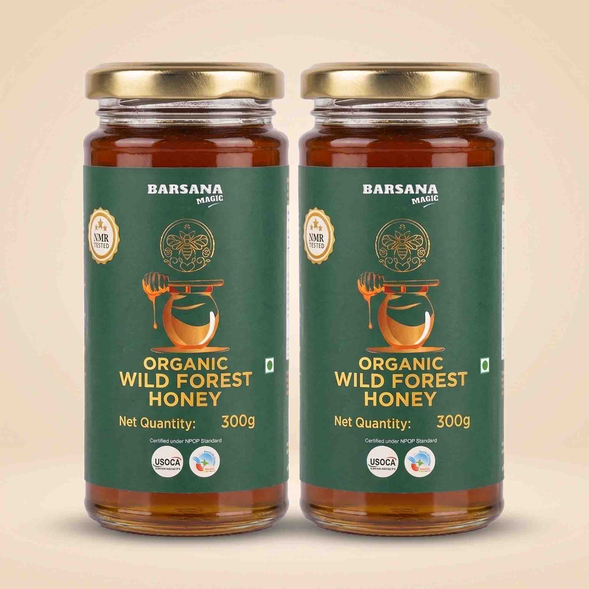 Barsana Magic and Two glass jars of Barsana Handmade Organic Wild Forest Honey with gold lids and dark green labels, displayed side-by-side on a light beige background.